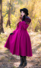 Obraz na płótnie Canvas Girl in a bright crimson coat walking in forest sunny autumn day