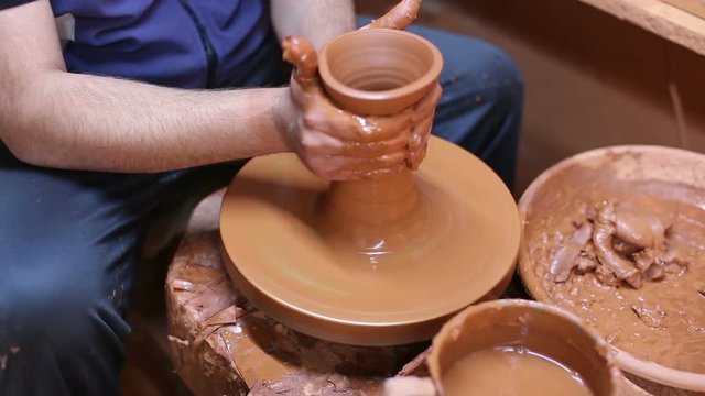 portrait of cheerful male potter working with clay on pottery wheel in atelier

