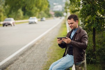 Obraz premium Man sitting on a road fence with gps tablet pc and using online maps