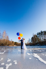 Bride and groom are walking at the surface of frozen lake with balloons