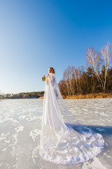 Bride is standing at the surface of frozen lake with long bridal veil