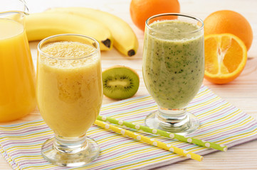 Healthy orange and kiwi smoothies with banana on white wooden background.