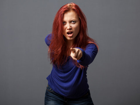 Young furious woman pointing the finger, gray background
