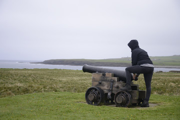 Obraz premium Girl shooting cannon Orkney coastline cliff landscape