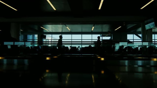 A huge cold in the airport terminal. Silhouettes of people who are in a hurry on a plane on the moving walkway, as well as the seat where your flight expected