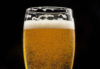 glass of beer with bubbles and foam on black closeup.