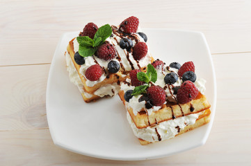 Belgian waffles with raspberries and blueberries on wooden backg