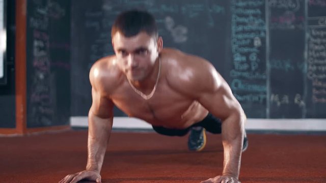 Muscular topless young man doing push ups in cross fit gym.