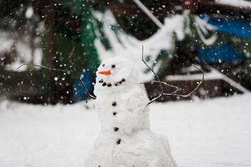 Hand built snowman in snowstorm with carrot nose, rocks for buttons and face and twigs for arms with fence and forest snowing snowflakes background 