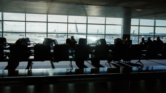 a large airport terminal on a sunny day. Silhouettes of people waiting for a flight, the aircraft through the window give the beautiful sun glare