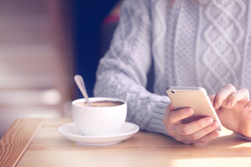Young woman with smartphone and cup of tasty coffee in cafe, closeup. Toned photo.