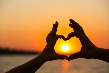 Silhouette of a male and a female hands in heart shape at sunset