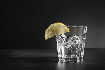 Glass of vodka with lemon and ice on dark background