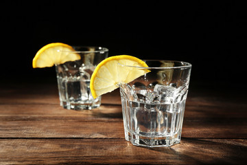 Glasses of vodka with lemon and ice on dark background