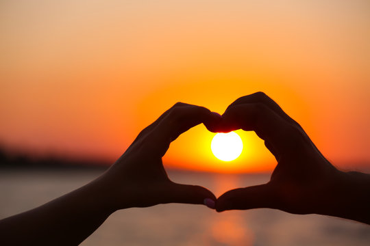 Silhouette of a male and a female hands in heart shape at sunset