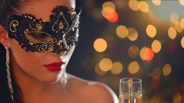 Beautiful sexy woman wearing venetian masquerade mask at party drinking champagne over holiday glowing background. Full HD 1080p video footage