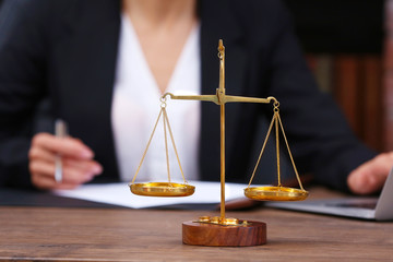 Scales of justice on wooden table and female lawyer on background