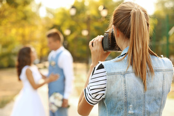 Young woman taking photo of happy wedding couple in park
