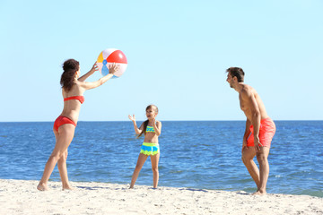 Family concept. Parents and daughter playing with ball on the beach