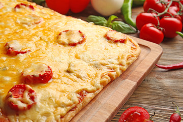 Delicious pizza with melted cheese on wooden cutting board, closeup