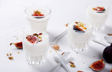 Yogurt in glass cups with nuts,pistachios and fresh figs.Breakfast,Dessert, Pudding on a white background.Food or Healthy diet concept.selective focus.Top view.