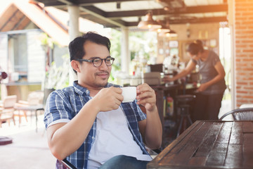 hipster man holding a cup of coffee while sitting at cafe lookin