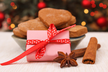 Wrapped gift, gingerbreads and christmas tree with lights in background