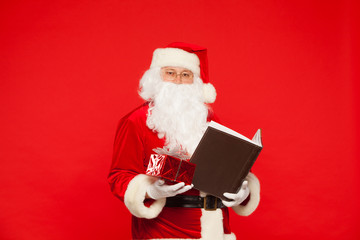 Naklejka premium Santa Claus reads old book, on a red background. Christmas