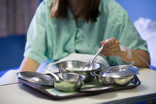Patient woman is on drip receiving a saline solution with cooked rice and other food in stainless bowl