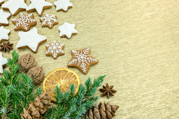 christmas gingerbread cookies with nuts, spices and fir tree branches on gold paper background