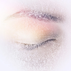 Naklejka premium Closed eyes with frost or snow on eyelashes macro close-up in winter on a beige background. Gentle romantic dreamy artistic image.