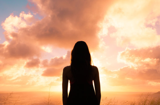 Young woman standing alone watching the sunset. 