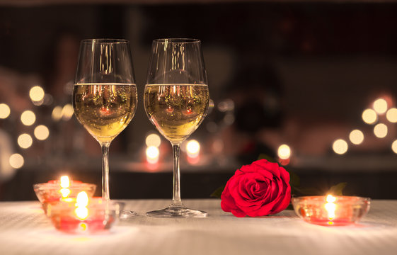 Romantic dinning concept. Pair of wine glasses on a table next to red rose. 
