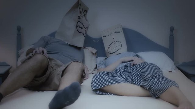 Two breadbag faces in the bed in the night, one is snoring while sleeping, the other is visibly angry.
