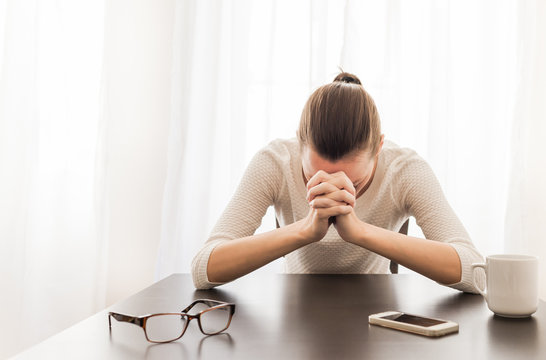 Young woman sitting in her office feeling desperate. Praying and emotion concept. 