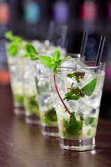 Row of four Mojito cocktails on a bar counter in a club. Vertica