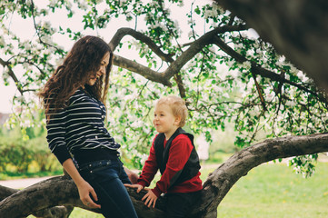 Naklejka na ściany i meble happy mother and toddler son playing together outdoor and climbing apple tree in spring or summer