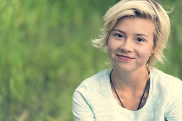 Portrait of a young blonde girl with a smile on blurred green background