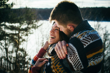 Joyful cute couple embraces. Young man in a sweater hugs a girl from behind background in winter. The concept of a successful relationship and happy moments