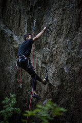 Outdoor sport. Rock climber dangles in midair as he struggles to climb a challenging cliff.