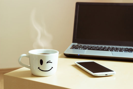 Smiling cup, smartphone and laptop on the desk