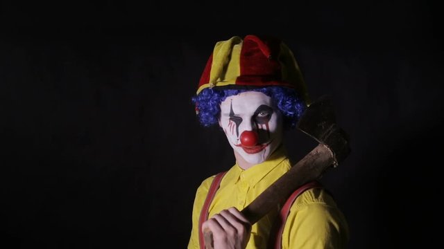 Scary clown with an axe in a dark room. Frightening jester, clown, buffoon. HD.