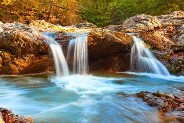 Beautiful waterfall in forest at sunset. Autumn landscape, fallen leaves, water flow 
