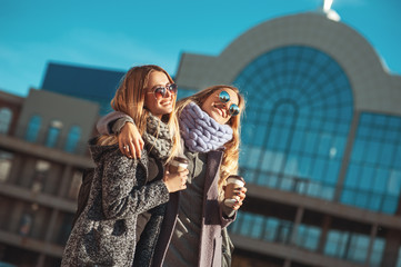 Two beautiful young women talking while walking the street after shopping holding the coffee and smiling. The weather is great today for walking with friend.