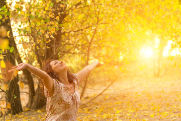 Adult brunette woman in a dress throws up dry leaves in the autumn forest in the sunlight
