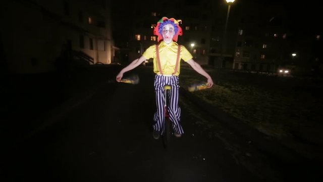 Sad scary clown riding on unicycles in a dark street. HD.