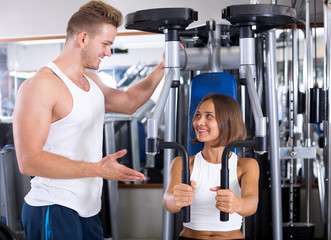 Man coach assisting woman in using pec deck