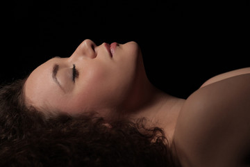 profile of a beautiful young woman with curly hair on dark background