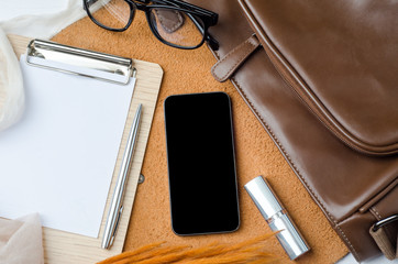 Wooden desktop with smart phone, leather bag, glasses and lipstick