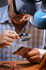 Male engineer checking board with magnifier